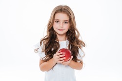 Довольно вьющиеся маленькая девочка стоя и держа красное яблоко над белым фоном