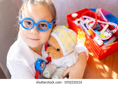 Pretty Cute Preschool Child Girl Wearing In White Medical Uniform Playing With Sick Teddy Bear Toy As Patient In Hospital Game