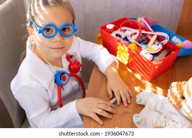 Pretty cute preschool child girl wearing in white medical uniform playing with sick teddy bear toy as patient in hospital game