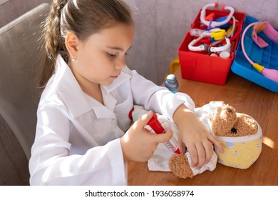 Pretty cute preschool child girl wearing in white medical uniform playing with sick teddy bear toy as patient in hospital game