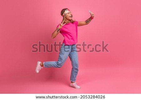 pretty cute smiling woman in pink shirt boho hippie style accessories smiling emotional fun posing on pink background isolated positive mood jumping holding phone