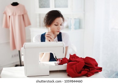 Pretty Cute young girl in a blue dress sews on a sewing machine.