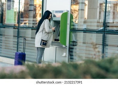 Pretty dark hair Caucasian woman with suitcase using ATM