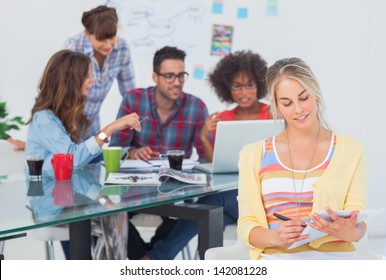 Pretty designer writing on a notepad with colleague brainstorming behind - Powered by Shutterstock