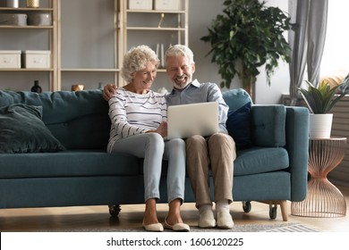 Pretty Elderly 70s Grey-haired Couple Resting On Couch In Living Room Hold On Lap Laptop Watching Movie Smiling Enjoy Free Time, Older Generation And Modern Wireless Technology Advanced Users Concept