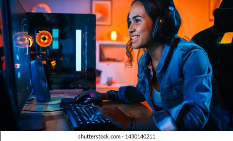 Pretty and Excited Black Gamer Girl in Headphones is Playing First-Person Shooter Online Video Game on Her Computer. Room and PC have Colorful Neon Led Lights. Cozy Evening at Home.