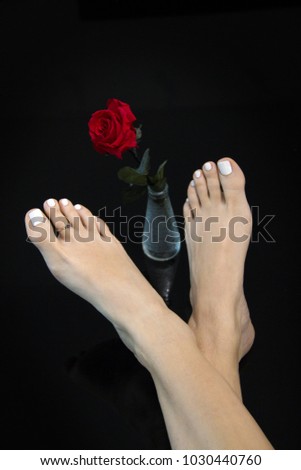 Pretty feet crossed and beautiful red rose in glass vase in the middle, woman foot on abstract black background, relaxing girl bare feet up on the black table