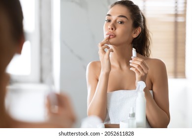 Pretty Female Applying Lip Balm Moisturizing Caring For Skin Standing Near Mirror In Modern Bathroom At Home. Makeup And Cosmetics, Lips Skincare Concept. Selective Focus