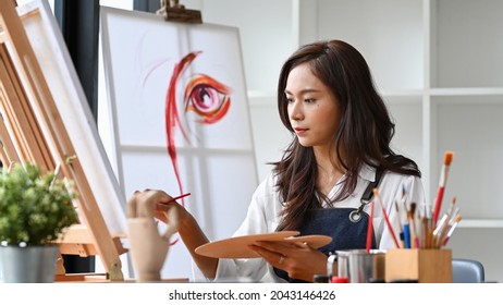 Pretty Female Artist Painting On Canvas In Bright Daylight Studio.