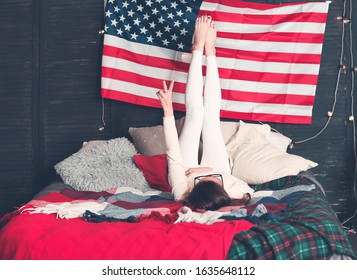 Pretty female in casualwear on bed with American flag on the wall during celebration of national Independence day  - Powered by Shutterstock