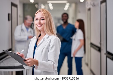 Pretty Female Doctor In White medical Unifrom with clipboard in hospital, standing in aisle, taking notes, checking information about patients, smile at camera - Shutterstock ID 1932915536