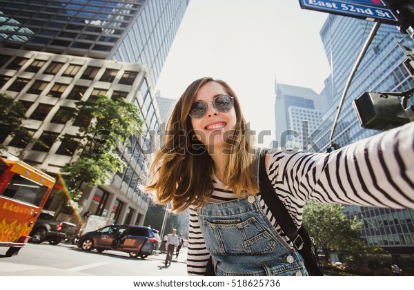 Pretty female girl tourist smiling and taking\
selfie in Manhattan, New York. Beautiful young photographer takes\
pictures for her travel\
blog.