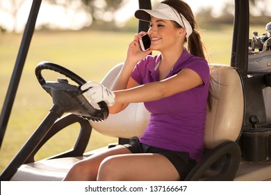Pretty female golfer talking on the phone while driving a golf cart