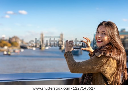 Pretty female London tourist is taking pictures of the Tower Bridge during her sightseeing trip through the city