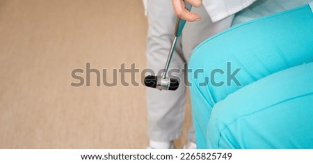 Pretty female orthopedist with patient in her office. Young doctor neurologist examining her patient with hammer. Neurologist checks the reflexes of a middle age female patient. Close up view.