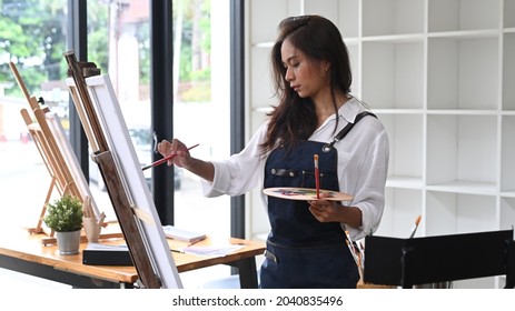 Pretty Female Painter Painting On Ease In Bright Daylight Studio.