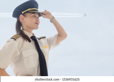 A pretty female pilot standing next to a airplane at the airport.