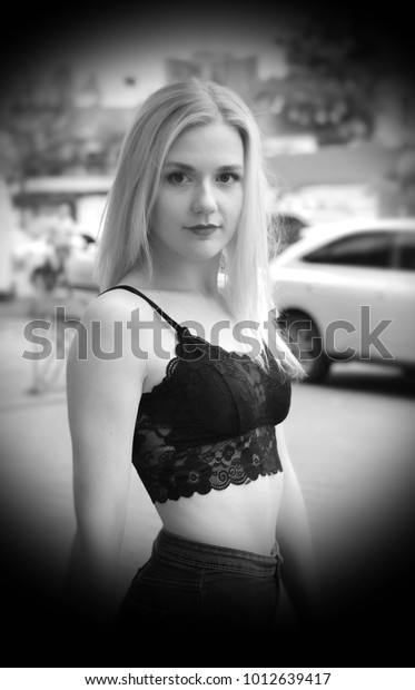Pretty\
female is posing on a street. Wearing blue jeans and black crop\
top. Near a shopping mall. Cars on the\
background.