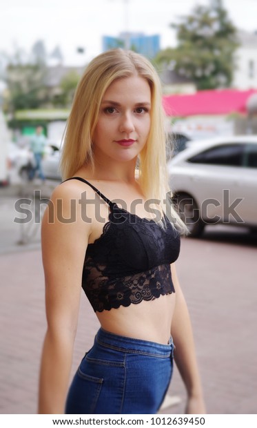 Pretty\
female is posing on a street. Wearing blue jeans and black crop\
top. Near a shopping mall. Cars on the\
background.