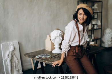 Pretty female sculptor 
				with beret and suspenders near table(authoring photo)