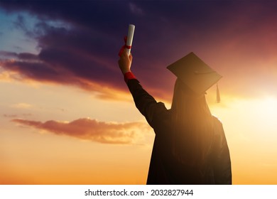 A pretty female student, celebrating her graduation and stand against the idyllic sunset view with holding her diploma high. - Powered by Shutterstock