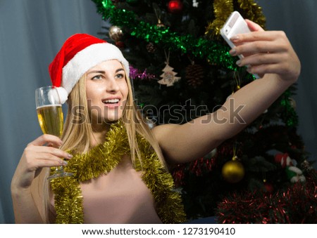 Pretty female is taking selfie with champagne in time celebration of New Year at home.