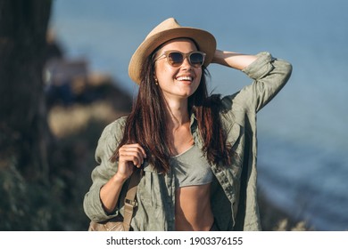 Pretty female traveler in hat and sunglasses with sea behind