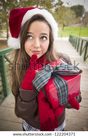 Pretty Festive Smiling Woman Wearing a Christmas Santa Hat with Wrapped Gift and Bow Outside.