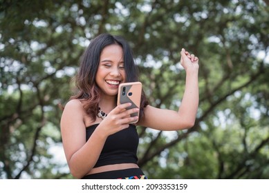 A Pretty Filipina Woman Celebrates Upon Seeing Great News On Her Phone. Receiving A Notification About Winning An Award Or Contest.