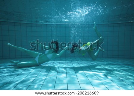 Pretty friends looking at camera underwater in bikinis in the swimming pool at the leisure centre