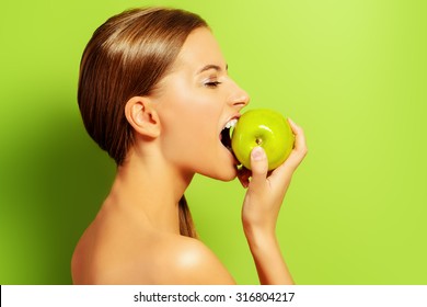 Pretty girl biting fresh apple over green background. Healthy lifestyle. Healthy eating. Fruits and vegetables. 