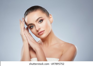 Pretty girl with brown hair fixed behind, clean fresh skin, big eyes and naked shoulders posing at gray studio background and looking at camera, holding hands near face, beauty photo. - Shutterstock ID 697895752