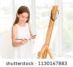 Pretty girl with brush in hand. Creative teen girl paitning a picture on easel. Girl practising drawing in art school
