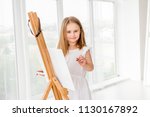 Pretty girl with brush in hand. Creative teen girl paitning a picture on easel. Girl practising drawing in art school