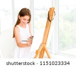Pretty girl with brush in hand. Creative teen girl paitning a picture on easel. Girl practising drawing in art school