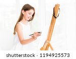 Pretty girl with brush in hand. Creative teen girl paitning a picture on easel. Girl practising drawing in art school