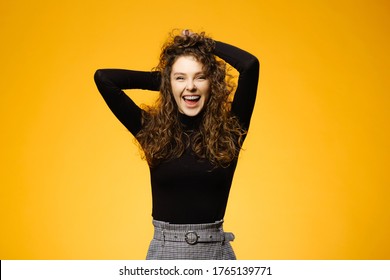 Pretty girl with curly hair isolated on yellow background. Model wearing long-sleeved shirt and smile for the camera