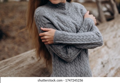 pretty girl dressed in a warm gray knitted sweater hugs herself in the park. gray knitted cashmere sweater on a beautiful girl. cold autumn. warm clothing