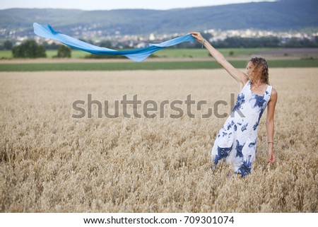 A pretty girl in the field with a blue flying scarf