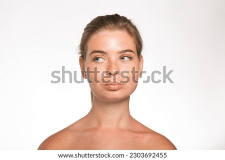 Pretty girl with freckles looks away with her hair tied up in front of the camera on a white background