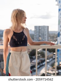 Pretty girl with freckles in a purple lace top and sweatpants. Posing on the balcony with his head thrown back. Against the background of a multi-colored multi-storey building.