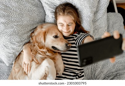 Pretty girl with golden retriever dog making selfie with smartphone in bed. Female teenager with purebred doggy pet labrador and mobile cell phone doing photos together - Powered by Shutterstock