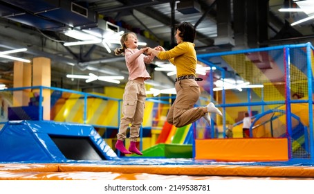 Pretty girl and her daughter kid jumping on colorful trampoline at playground park and smiling. Caucasian family happy during active entertaiments - Shutterstock ID 2149538781