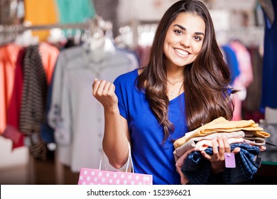 Pretty girl holding a shopping bag and some clothes she wants to try on at a clothing store - Powered by Shutterstock