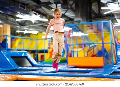 Pretty girl kid jumping on colorful trampoline at playground park and smiling. Caucasian preteen child during active entertaiments indoor - Shutterstock ID 2149538769