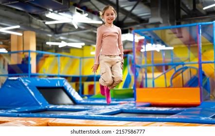 Pretty girl kid jumping on colorful trampoline at playground park and smiling. Beautiful preteen child during active entertaiments - Shutterstock ID 2157586777