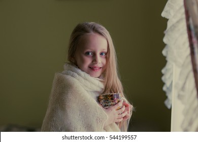 Pretty girl with long flowing hair in a scarf with a mug at the window. Vintage processing

