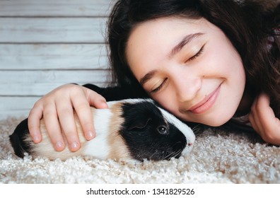 Pretty girl looks at the guinea pig and rejoices meeting and stroking her. Boss and pet. Love between man and animal. Happy shopping. A touching photo.