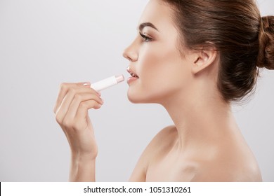 Pretty girl with nude make up and naked shoulders posing at grey background, skin care concept, beauty photo, close up portrait, using lipstick. 