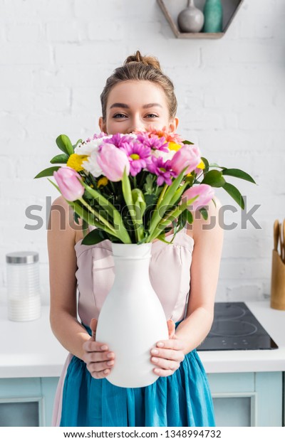 pretty girl with obscure face hiding behind bouquet\
of wildflowers in vase